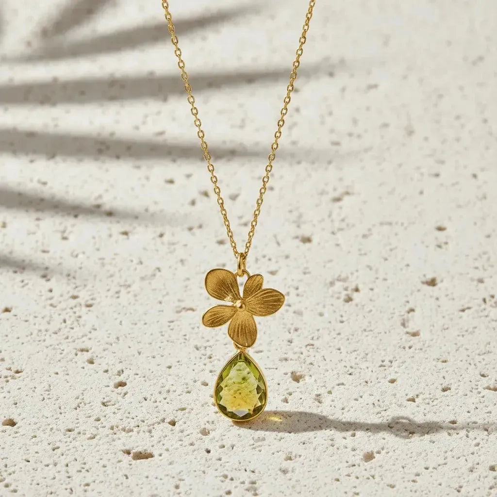 Gold necklace with a green teardrop pendant on a textured beige surface
