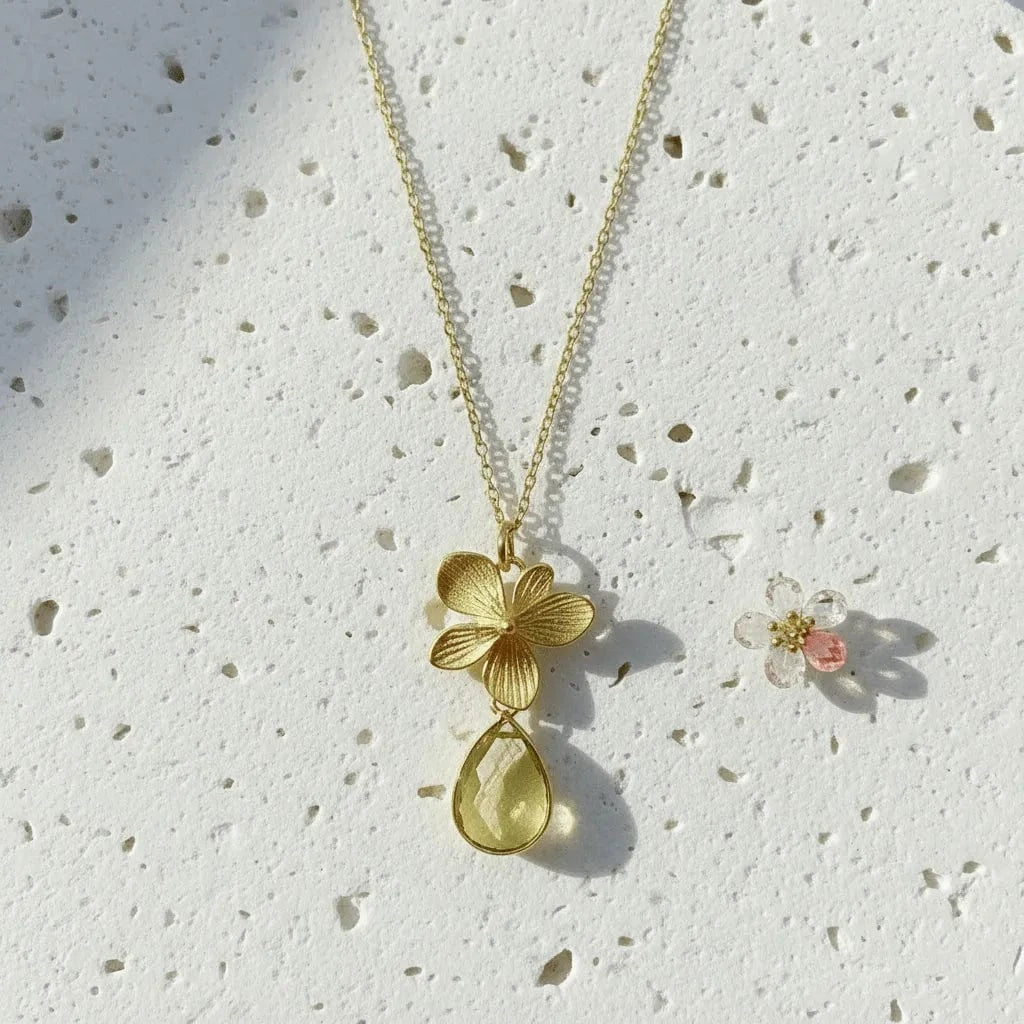 Gold necklace with floral pendant on a textured white surface