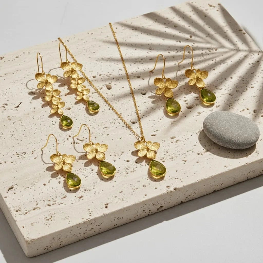 Gold jewelry set with floral designs and green stones on a textured stone surface.