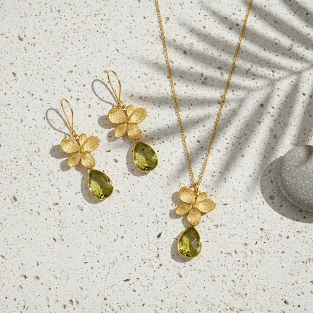 Gold necklace and earrings with green teardrop pendants on a textured surface