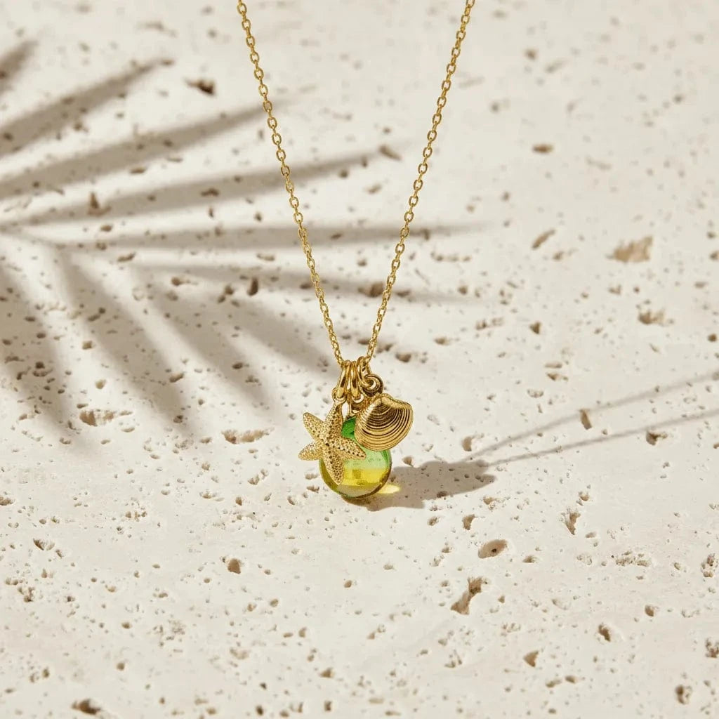 Gold necklace with a green pendant on a beige surface