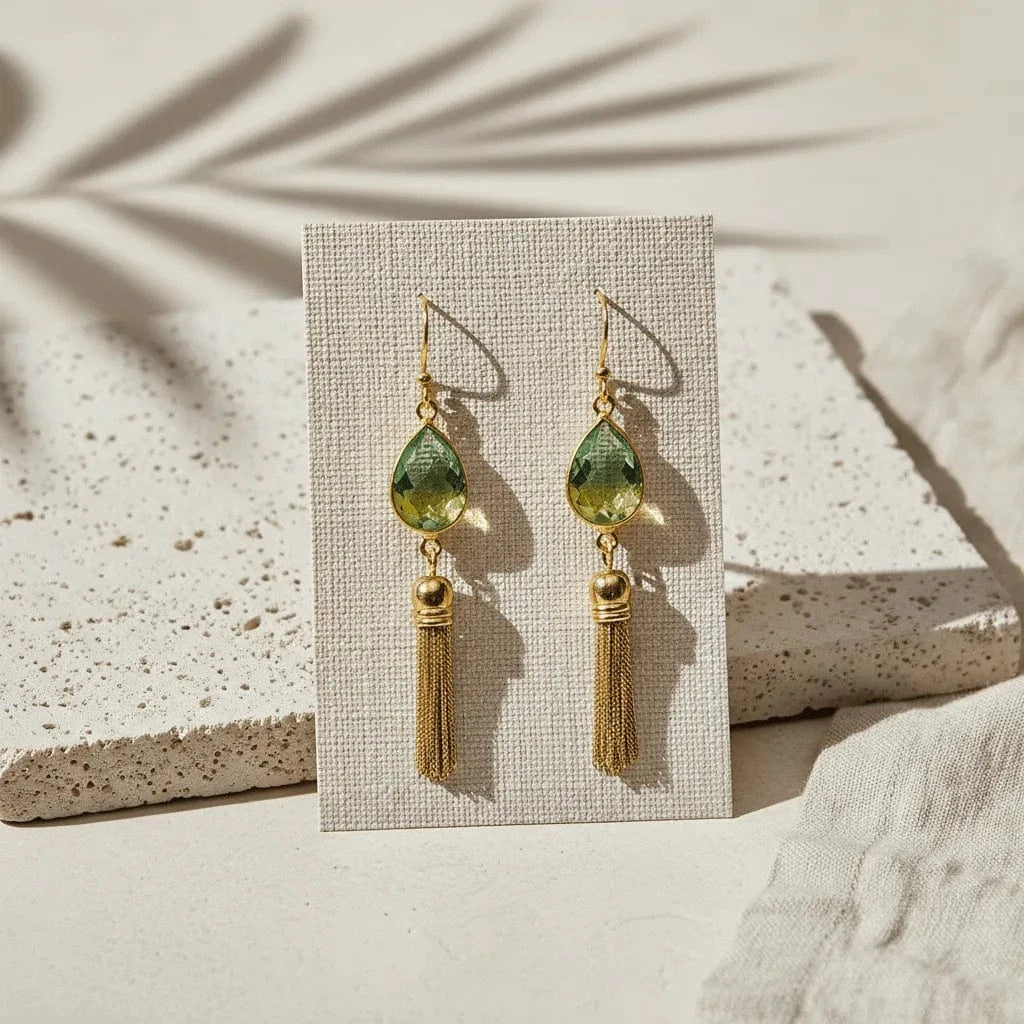 Gold earrings with green teardrop-shaped beads and tassels on a beige background