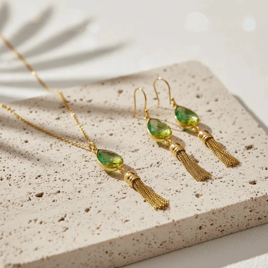 Gold earrings with green teardrop-shaped stones on a textured surface