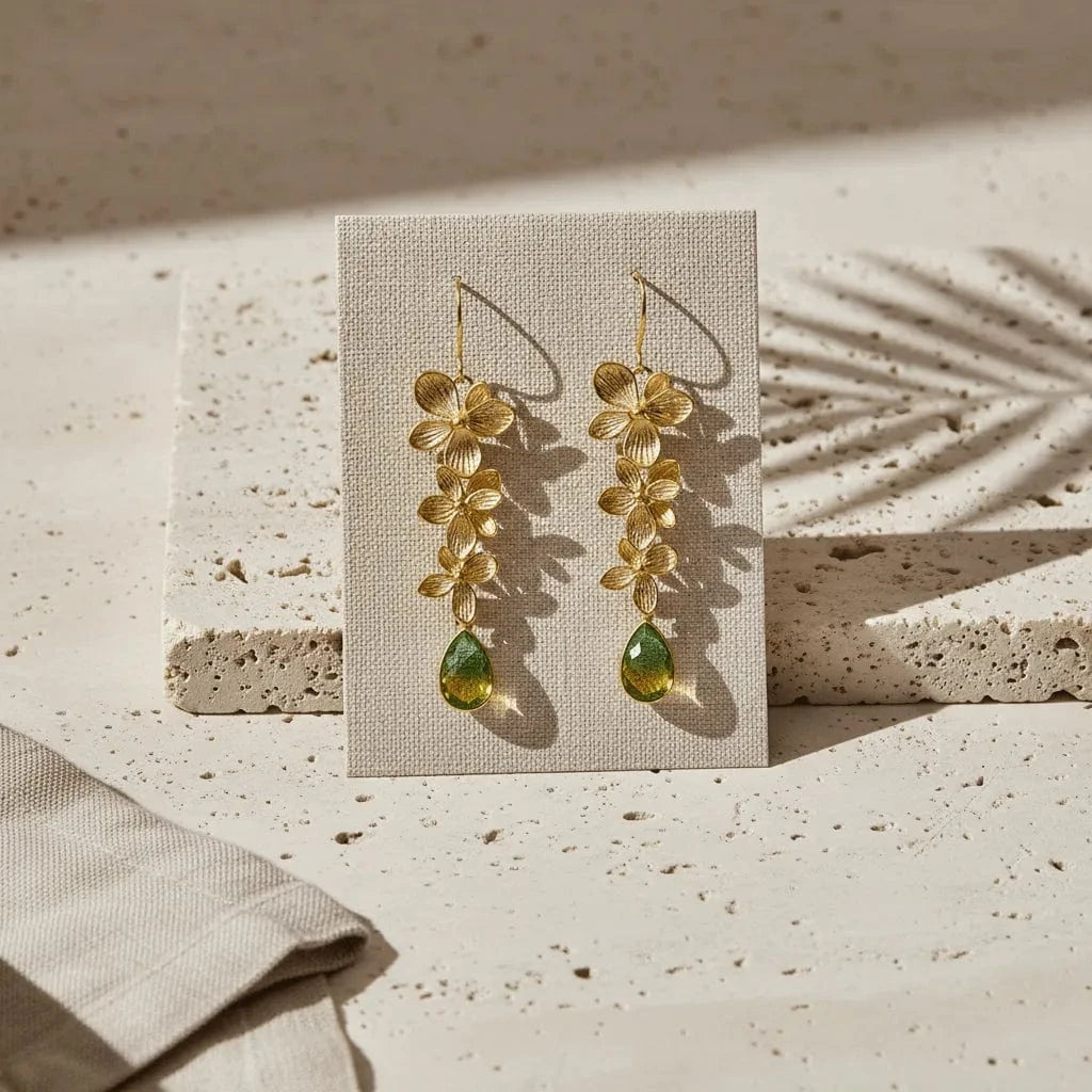 Gold floral earrings with green drops on a beige card against a textured beige background