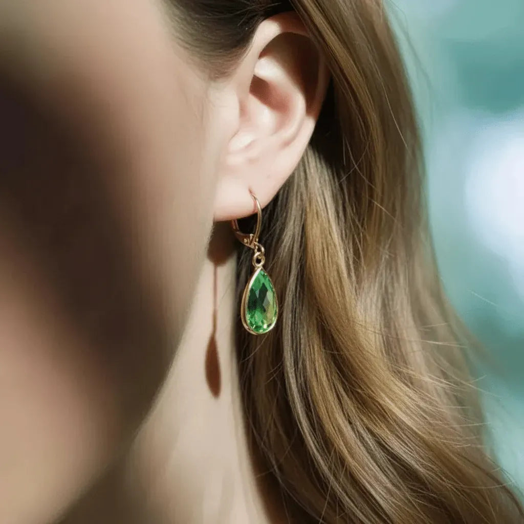 Close-up of a woman wearing a green teardrop earring with a blurred background