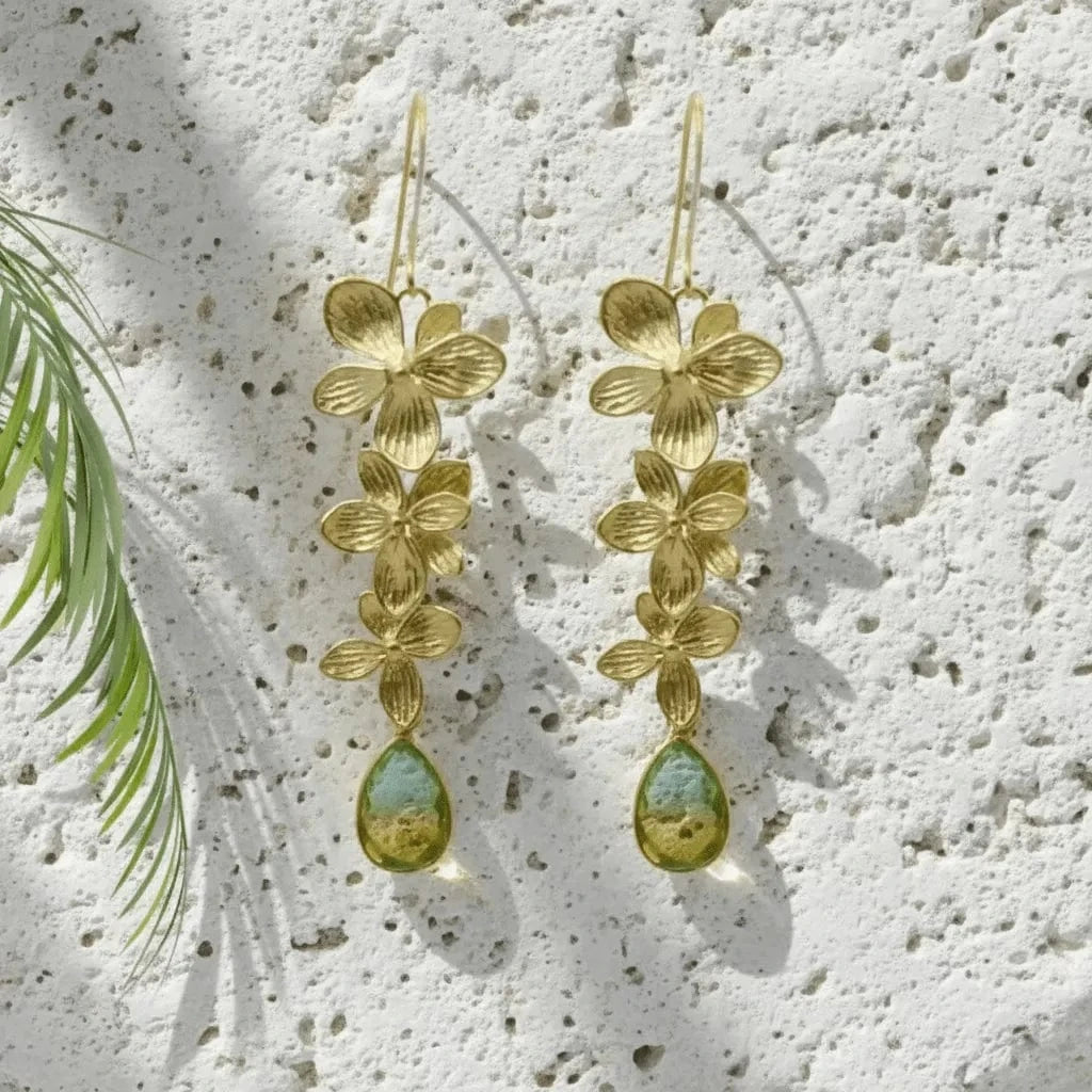 Gold floral earrings with green teardrop stones on a textured white surface.