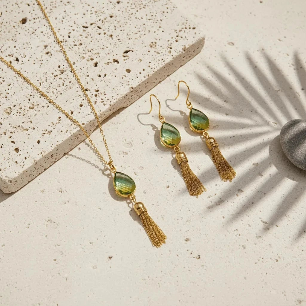 Jewelry set with necklace and earrings featuring teardrop-shaped green stones and gold tassels on a white background.