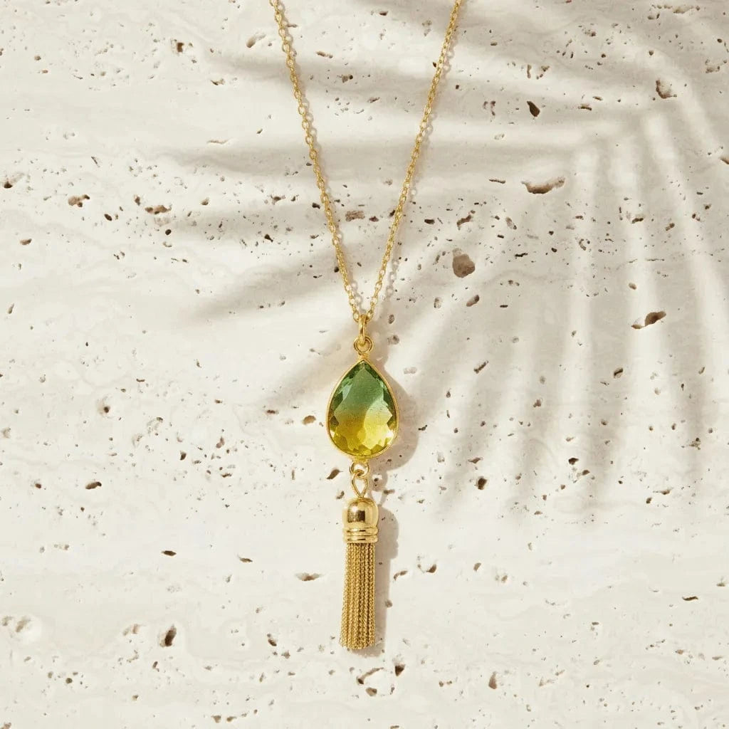 Necklace with a green teardrop pendant and gold tassel on a textured beige background