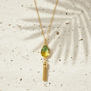Necklace with a green teardrop pendant and gold tassel on a textured beige background