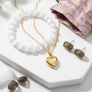 Gold heart-shaped pendant necklace with matching earrings on a white surface.