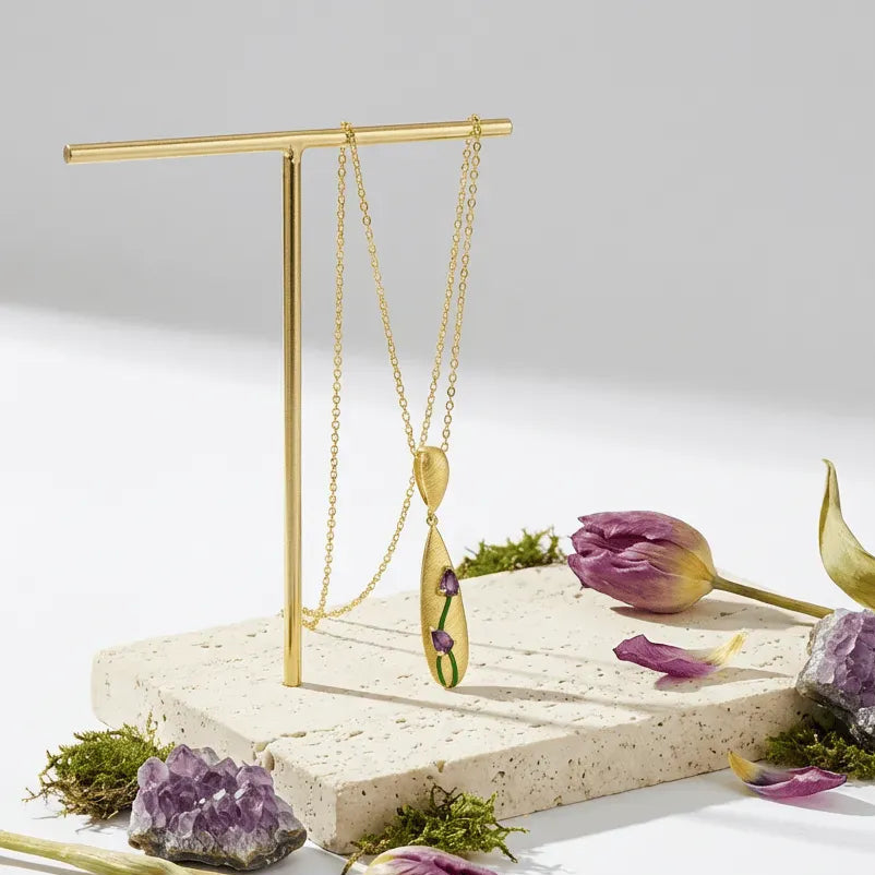 Tulip Amethyst Necklace displayed on a stand with flowers and stones on a light background