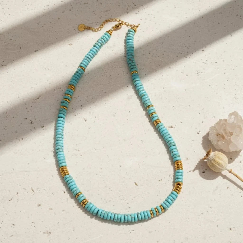 Turquoise beaded necklace with gold accents on a white background