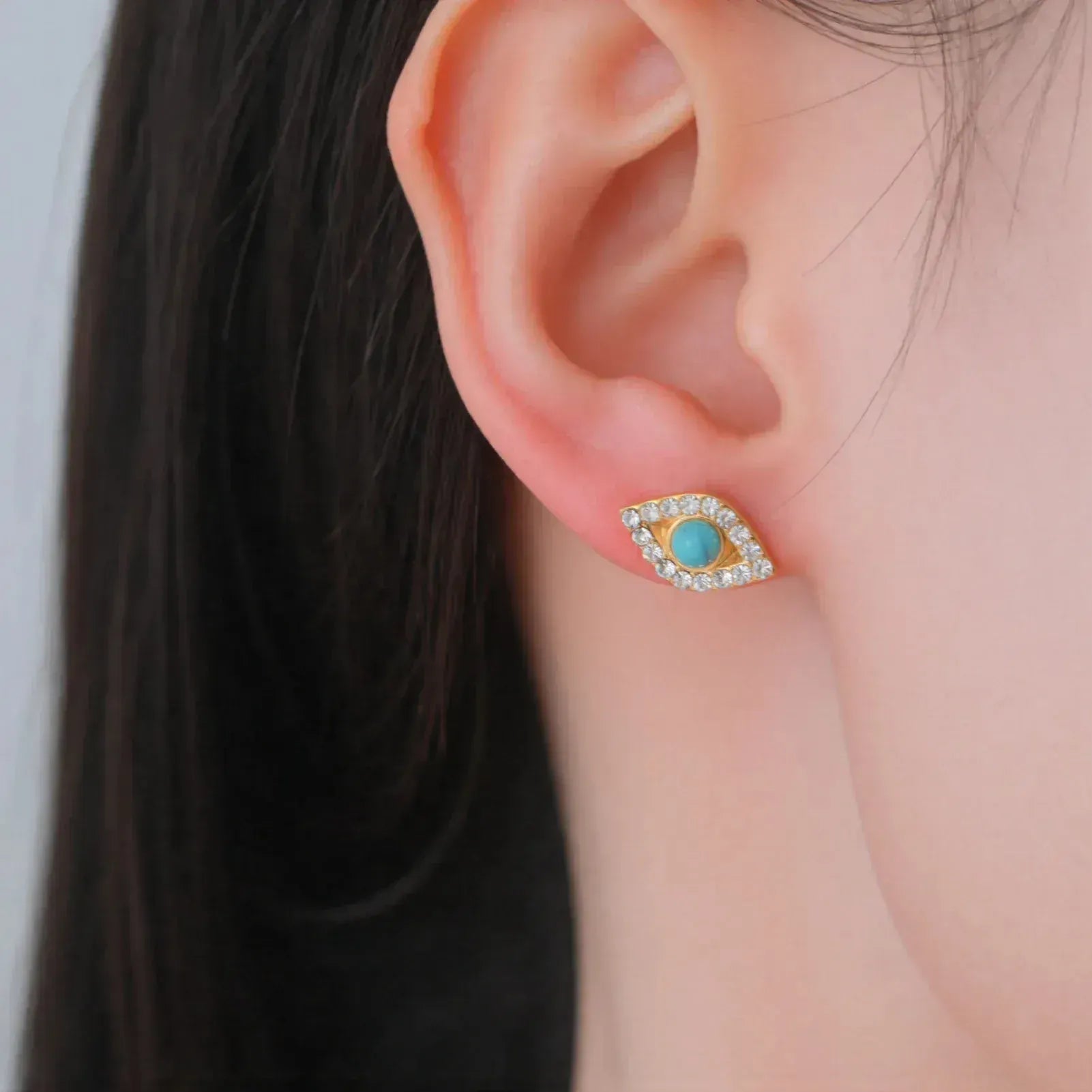 Close-up of an ear wearing a turquoise stud earring with a gold setting.