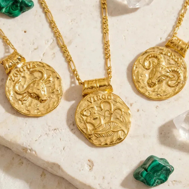 Gold zodiac pendants on chains with gemstones on a textured surface
