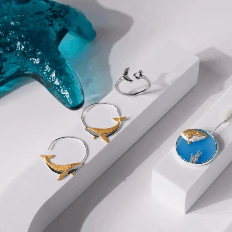 Jewelry set with dolphin-themed rings and a blue pendant on a white surface.