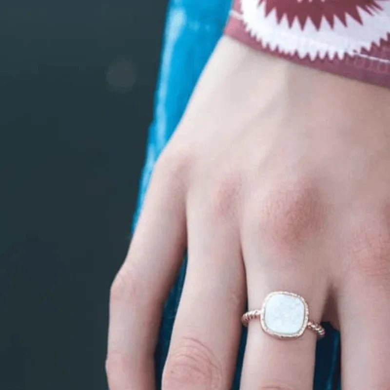 Close-up of a hand wearing a rose gold ring with a white stone on a blurred background