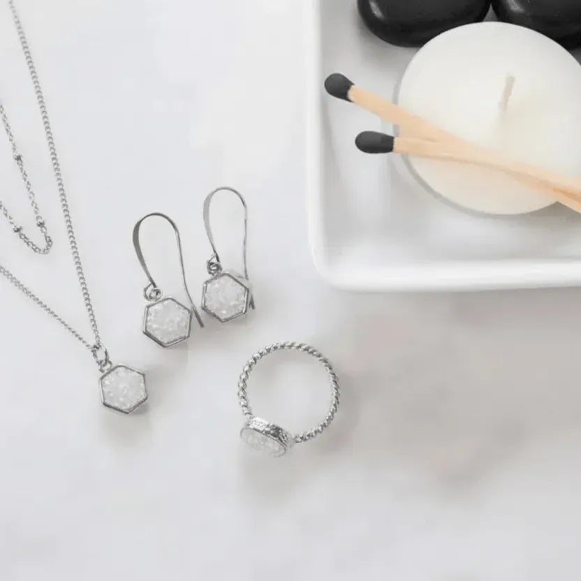 Silver jewelry set with necklace, earrings, and ring on a white surface with candles and matches.