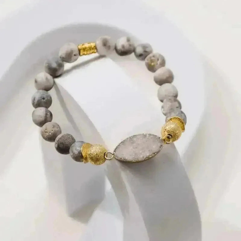 Bracelet with gray beads and gold accents on a white stand