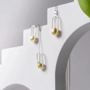 Pair of silver and gold earrings on a white stand with a gray background