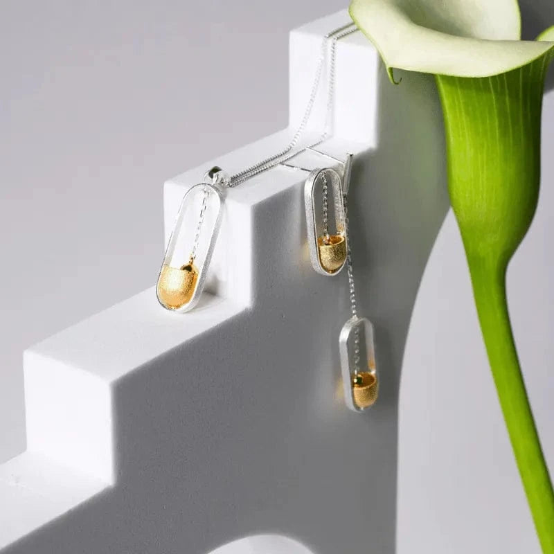 Gold and silver earrings on a white stand with a green flower.