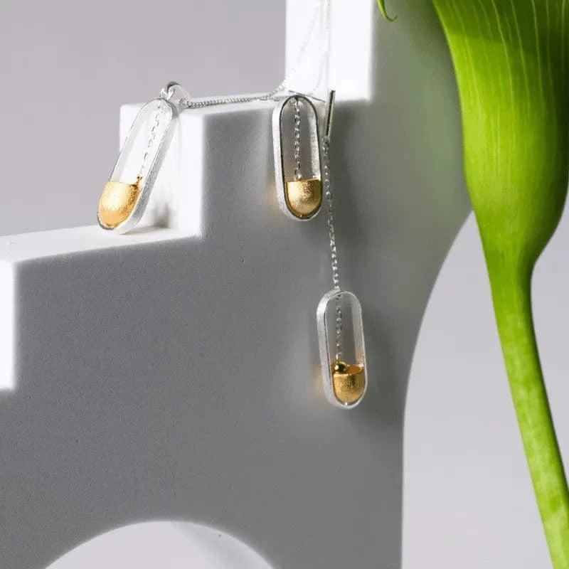 Earrings with gold and silver droplet designs on a white surface with a green leaf.