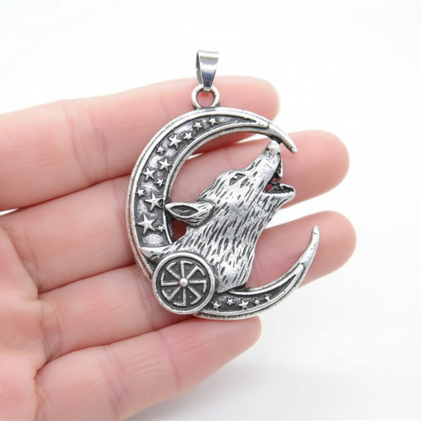 Silver wolf and moon pendant held in a hand with a green grass background