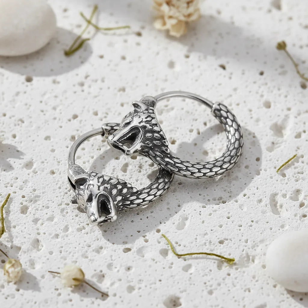 Pair of silver hoop earrings with detailed designs on a textured white surface.