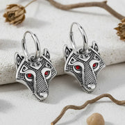 Silver horse head earrings with red eyes on a textured surface.