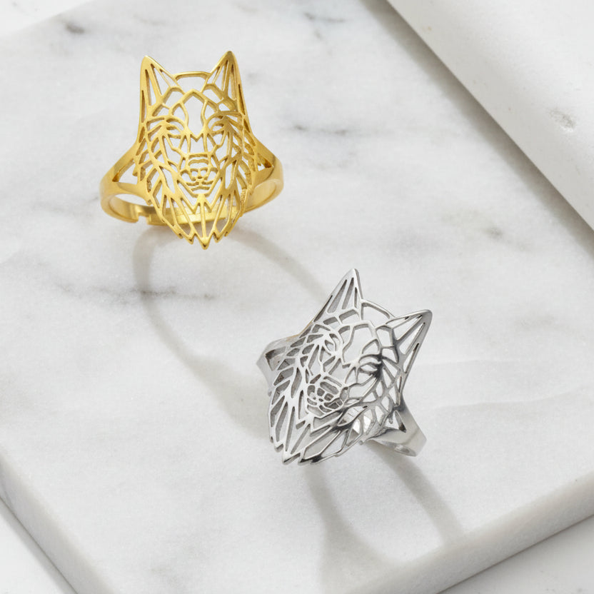 Gold and silver wolf head rings on a green surface