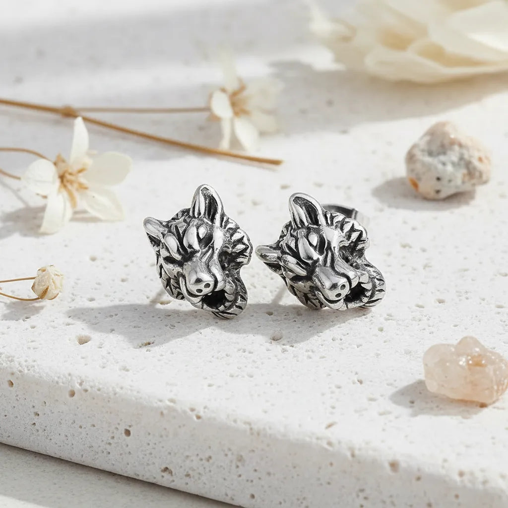 Silver wolf head earrings on a textured white surface with dried flowers.