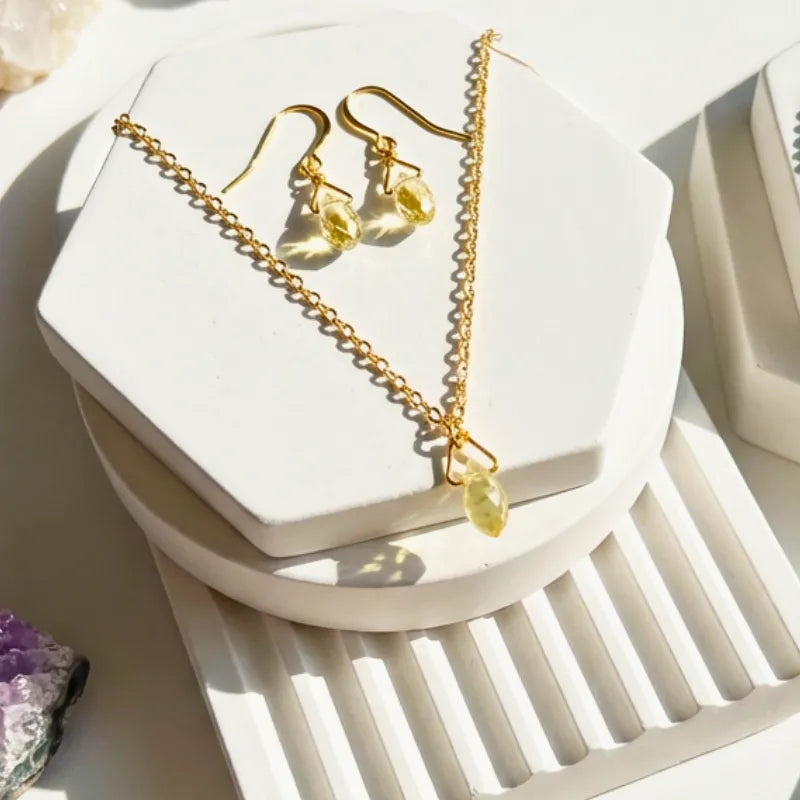 Dainty yellow faceted Swarovski crystal drop necklace and matching earrings on gold-plated chain, displayed on white hexagonal stand
