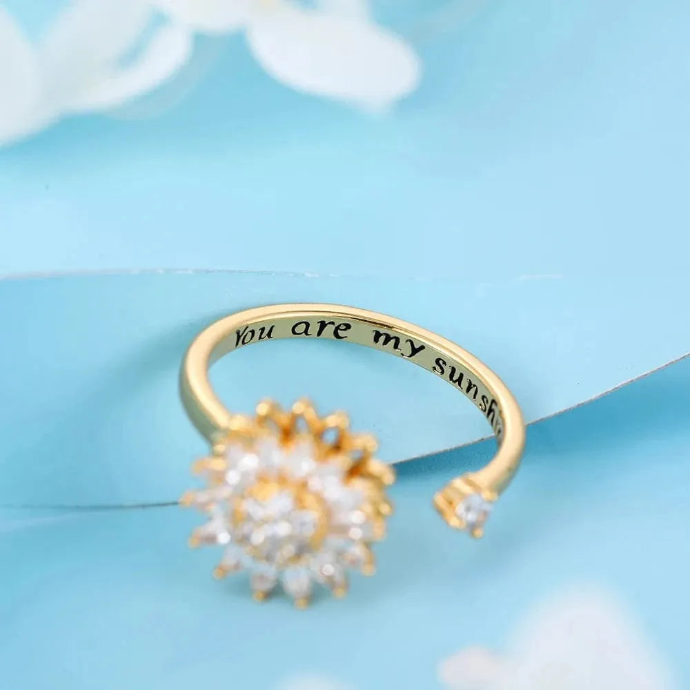 Gold ring with pearl-like stones and 'You are my sunshine' engraving on a light blue background