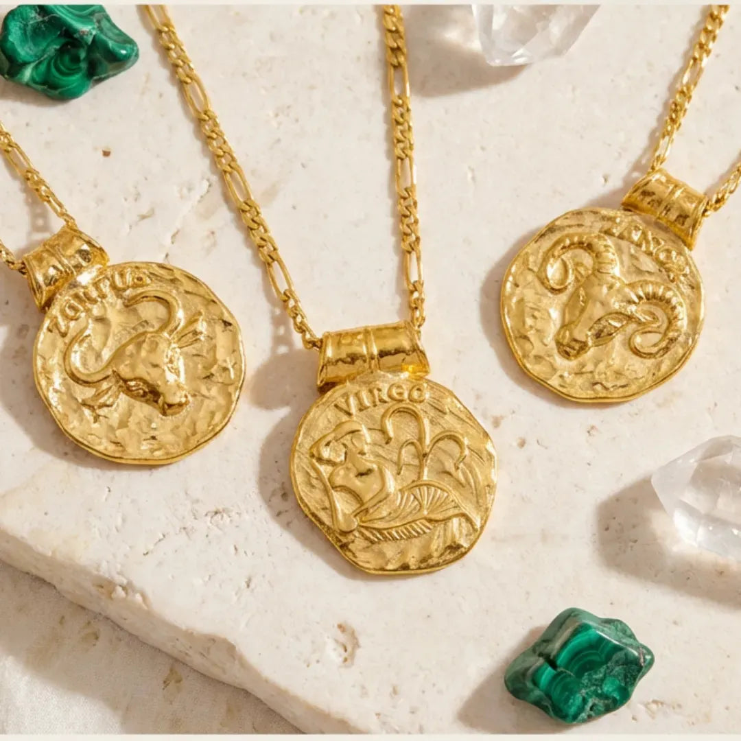 Gold zodiac pendants on chains with gemstones on a textured surface