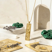 Gold pendant necklace on a table with tarot cards, lavender, and green crystals.